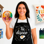 Mujer mediterránea sonriente con camiseta blanca y delantal negro con diseño de utensilios de cocina y texto “Tu diseño”, sosteniendo un reloj de cocina con la foto de una señora sacando la lengua. ademas se ven diferentes productos personalizados.